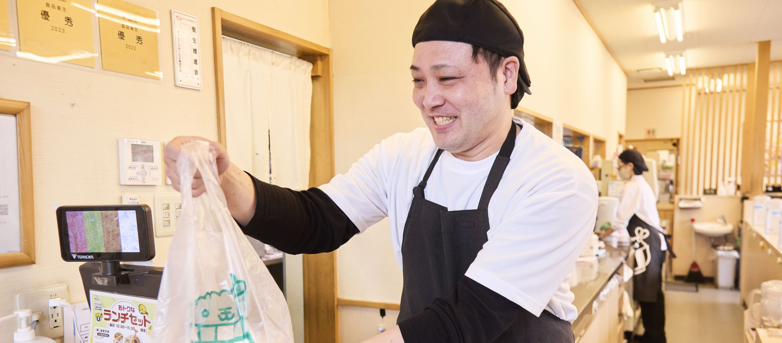 お持ち帰りの料理をお渡しするさん天店長